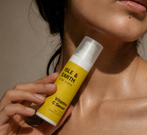 Woman with glowing skin holding Isle & Earth Vitamin C Serum yellow bottle against her neck and jaw