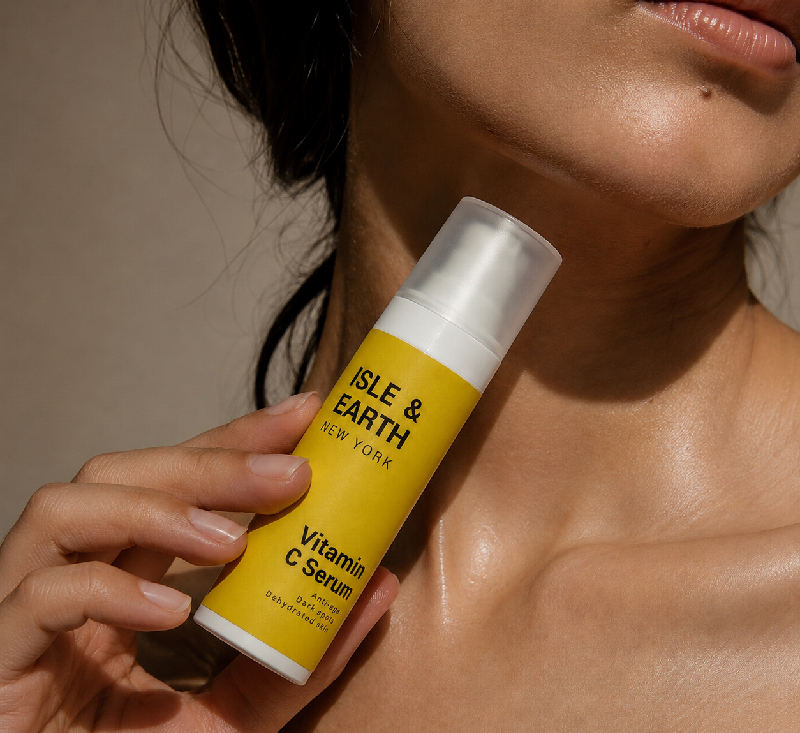 Woman with glowing skin holding Isle & Earth Vitamin C Serum yellow bottle against her neck and jaw