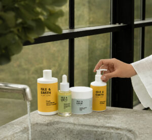 Woman's hand reaching for Isle & Earth Moisturising Shampoo beside Fresh Conditioner Citrus Cocktail, Rosemary Hair Oil, and Icelandic Volcano Scrub on a stone bathroom shelf