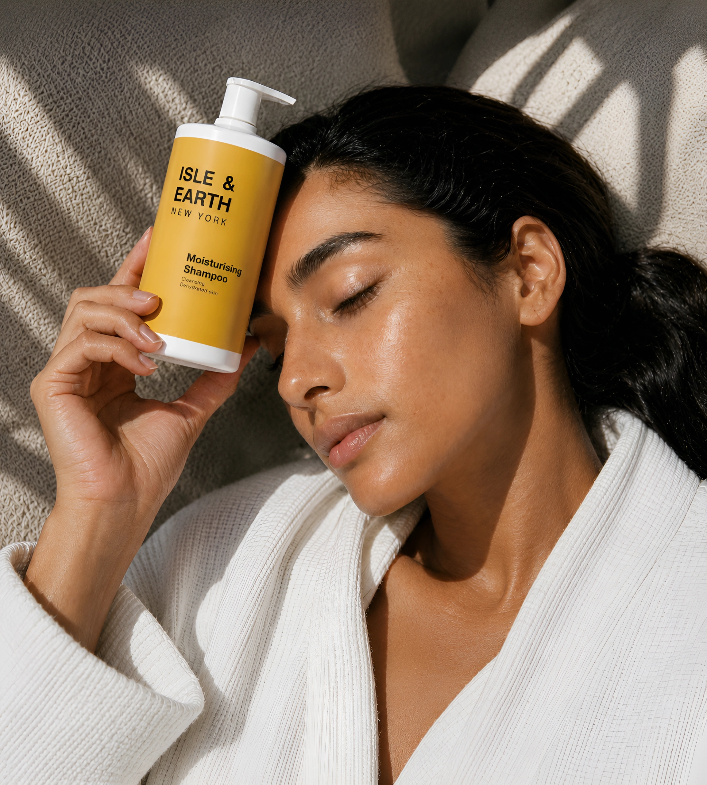 Woman in white robe holding Isle & Earth Moisturising Shampoo bottle with eyes closed in natural sunlight