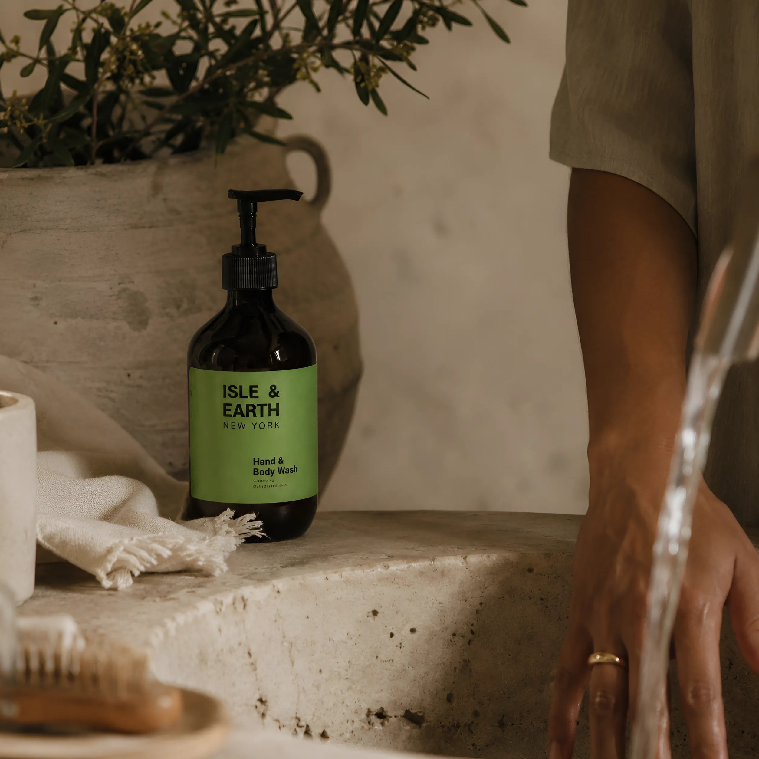 Isle & Earth Ginger Cardamom Hand & Body Wash amber bottle on stone surface with botanical greenery and linen cloth in natural light